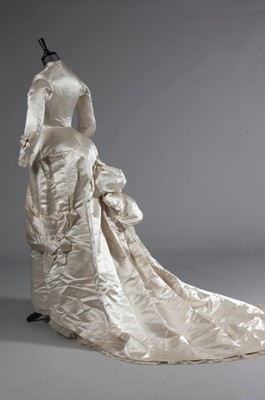 Lot 55 - An ivory satin bridal gown, late 1870s, of...